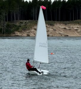 Sailor navigating small boat on calm lake with trees