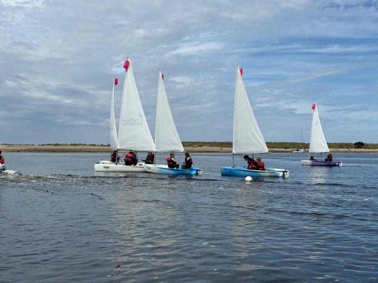 Children sailing small dinghies on calm estuary