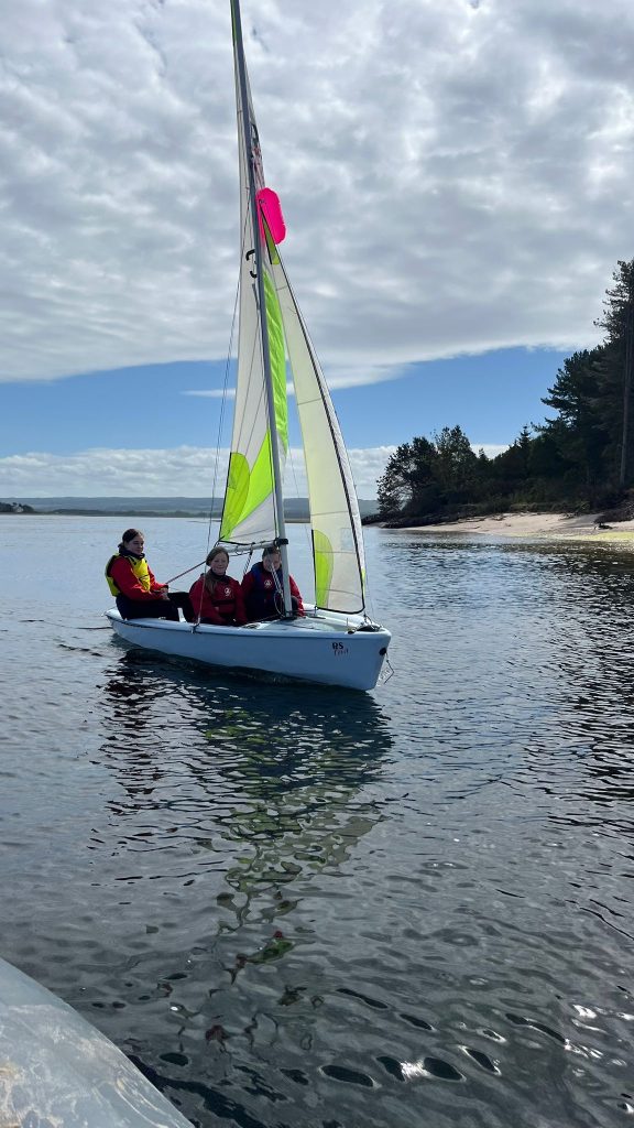 Three children sailing dinghy on calm coastal water