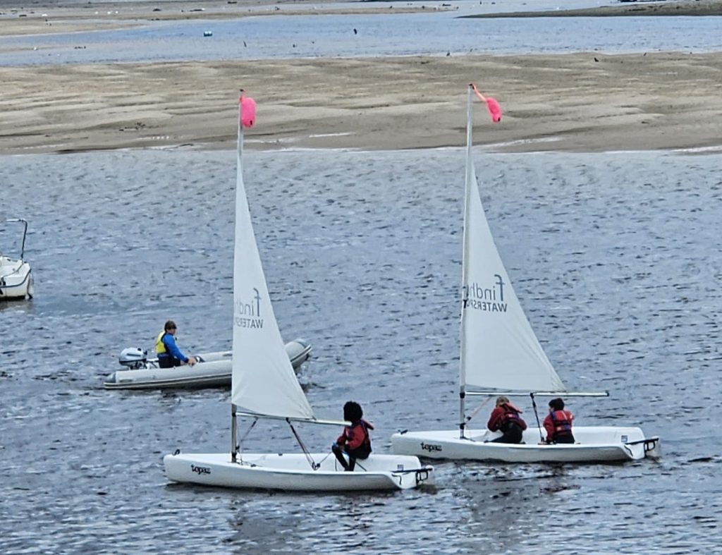 Children sailing dinghies with instructor on calm water