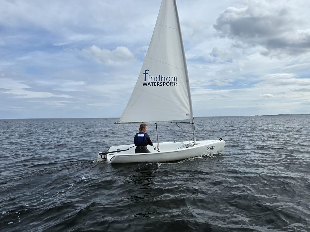 Person sailing dinghy on calm sea under clouds