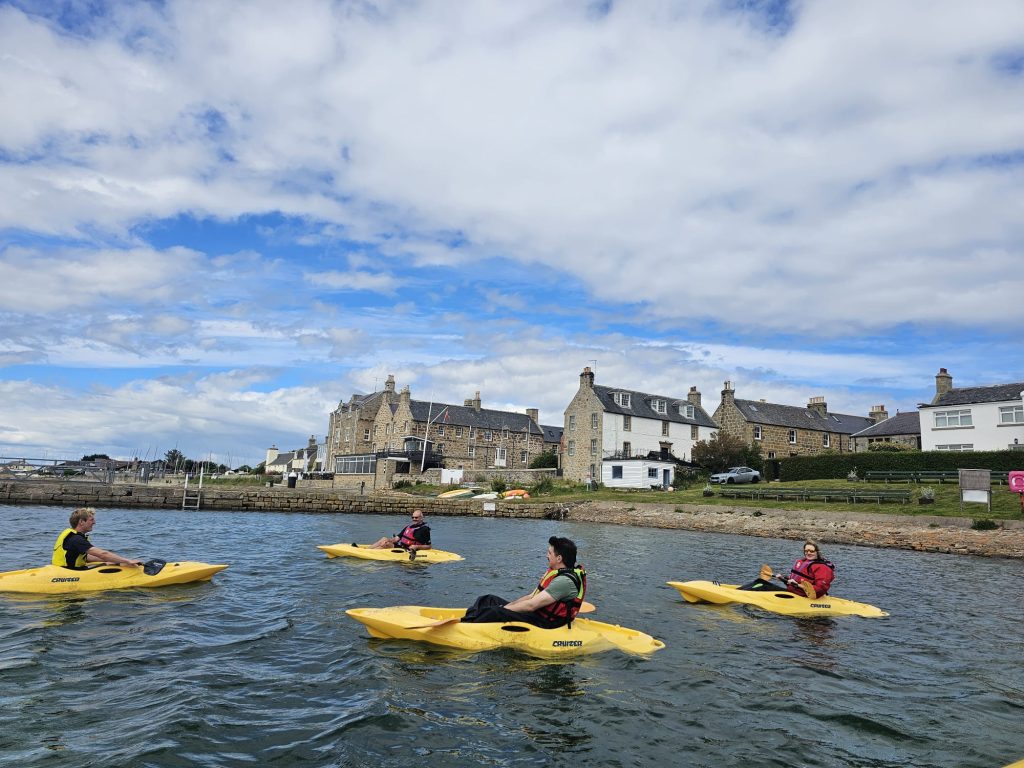 People kayaking near stone houses by harbour