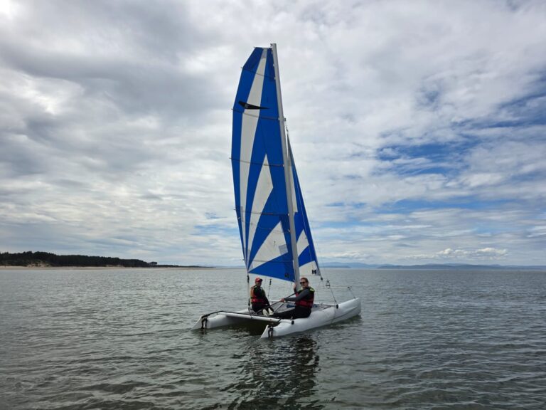 Two people sailing a blue-and-white catamaran