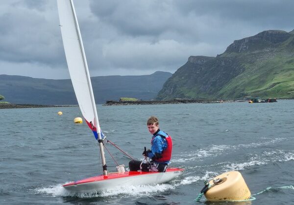 Young man sailing dinghy in mountainous coastal waters