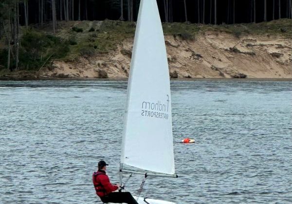 Person sailing small boat on tranquil lake near forest