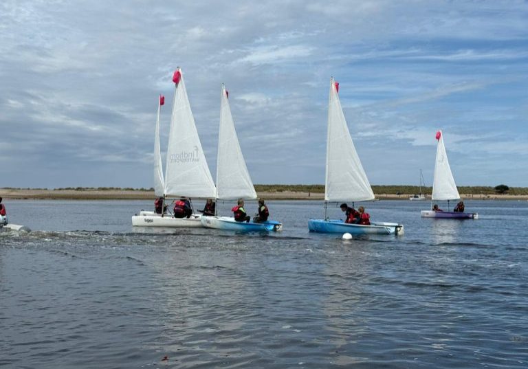 Children sailing small dinghies on calm estuary