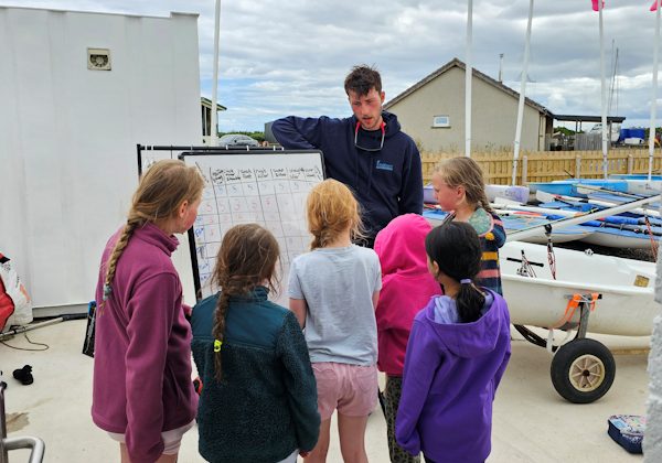 Instructor explaining sailing techniques to children at marina