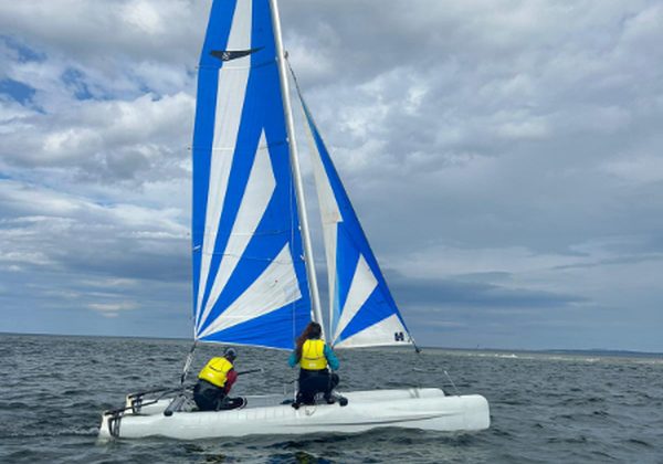 Two people sailing a catamaran with blue sails