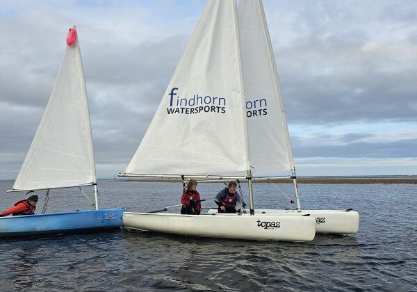 Sailboats with people on calm water, Findhorn Watersports logos