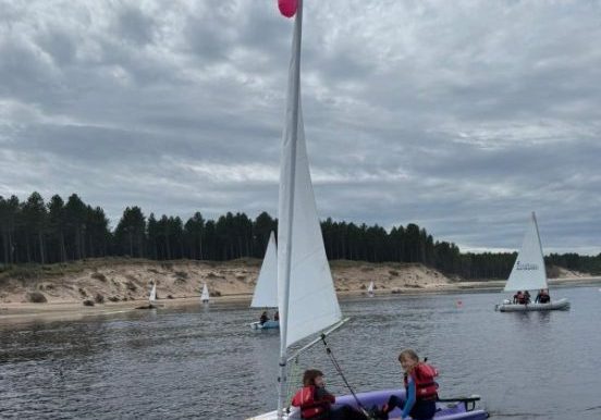 Children sailing dinghy on cloudy lake with other boats