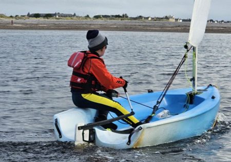 Person sailing a small blue boat in coastal waters