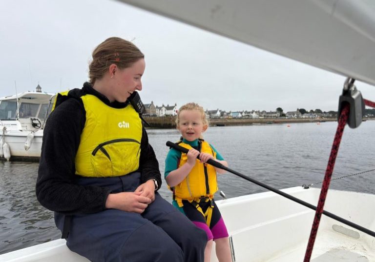 Two people wearing life jackets in a sailboat