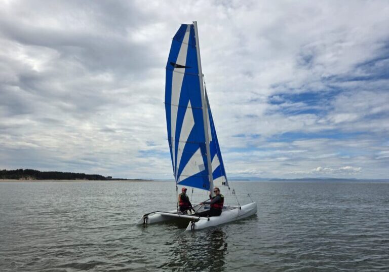 Two people sailing a blue-and-white catamaran